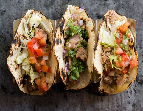 Four tacos on a tray, topped with cilantro, onion, and salsa fresca